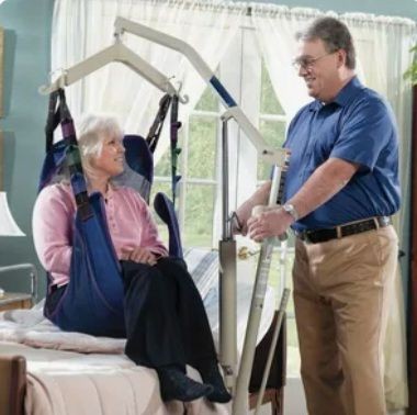 Person assisting another person using a lift mechanism in a room with bright windows and curtains.